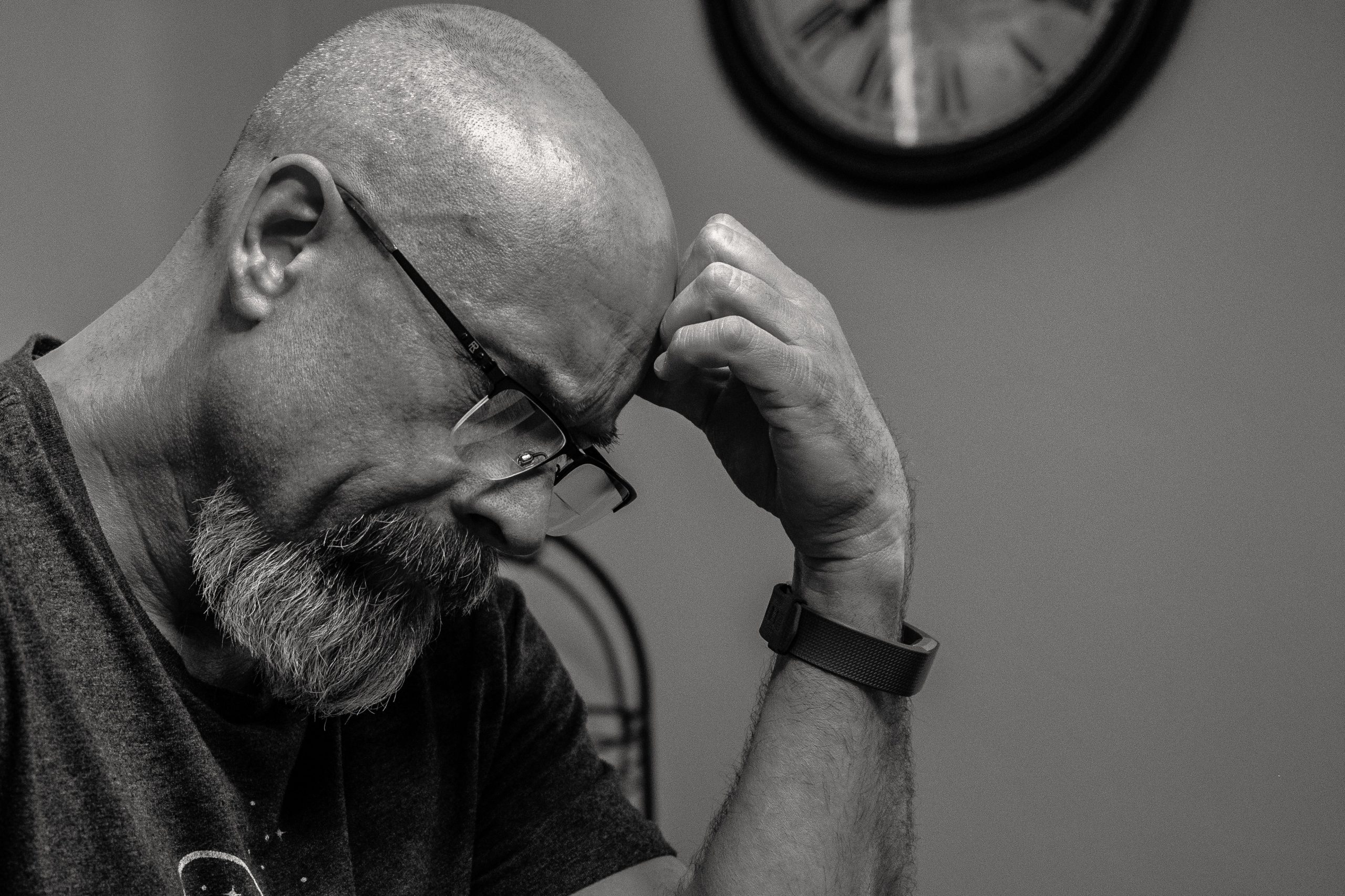 A man resting his head on his hand, looking stressed, beneath a wall clock